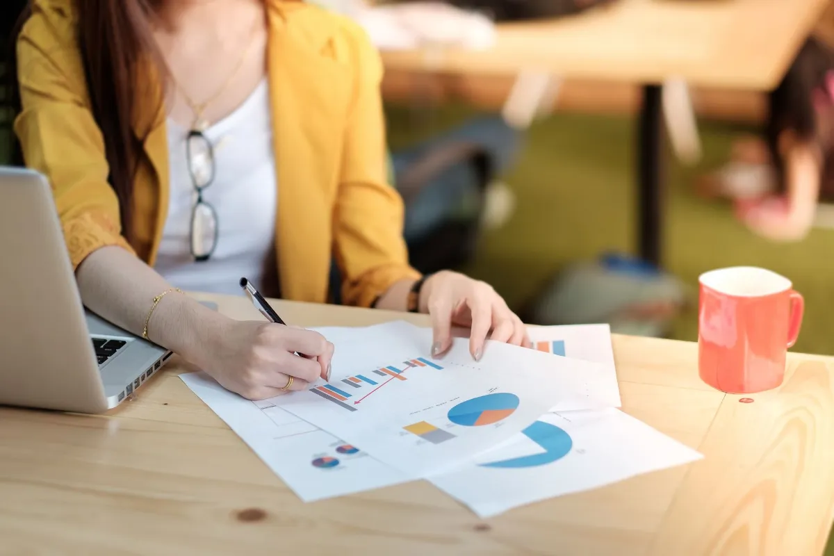 business woman analyzing investment charts with laptop on wooden desk.